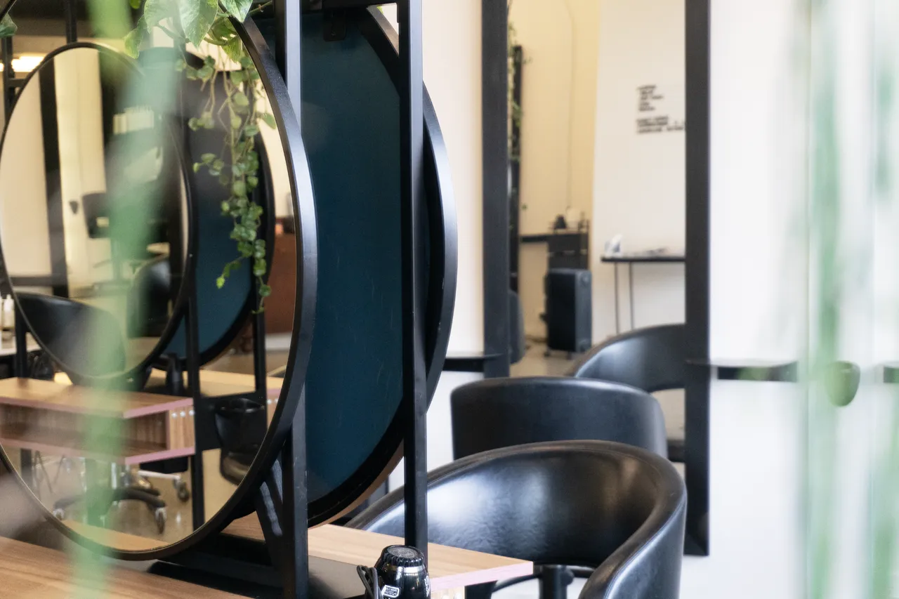 A leather styling chair framed by a round mirror and greenery